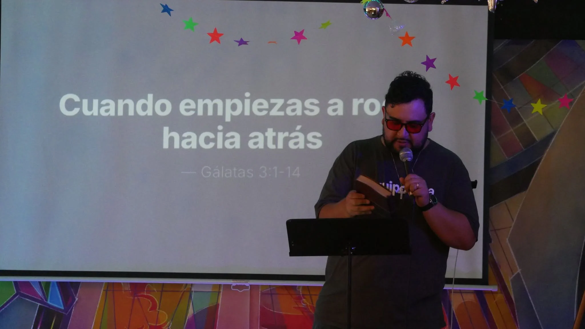 El pastor predicando con micrófono frente a la pantalla